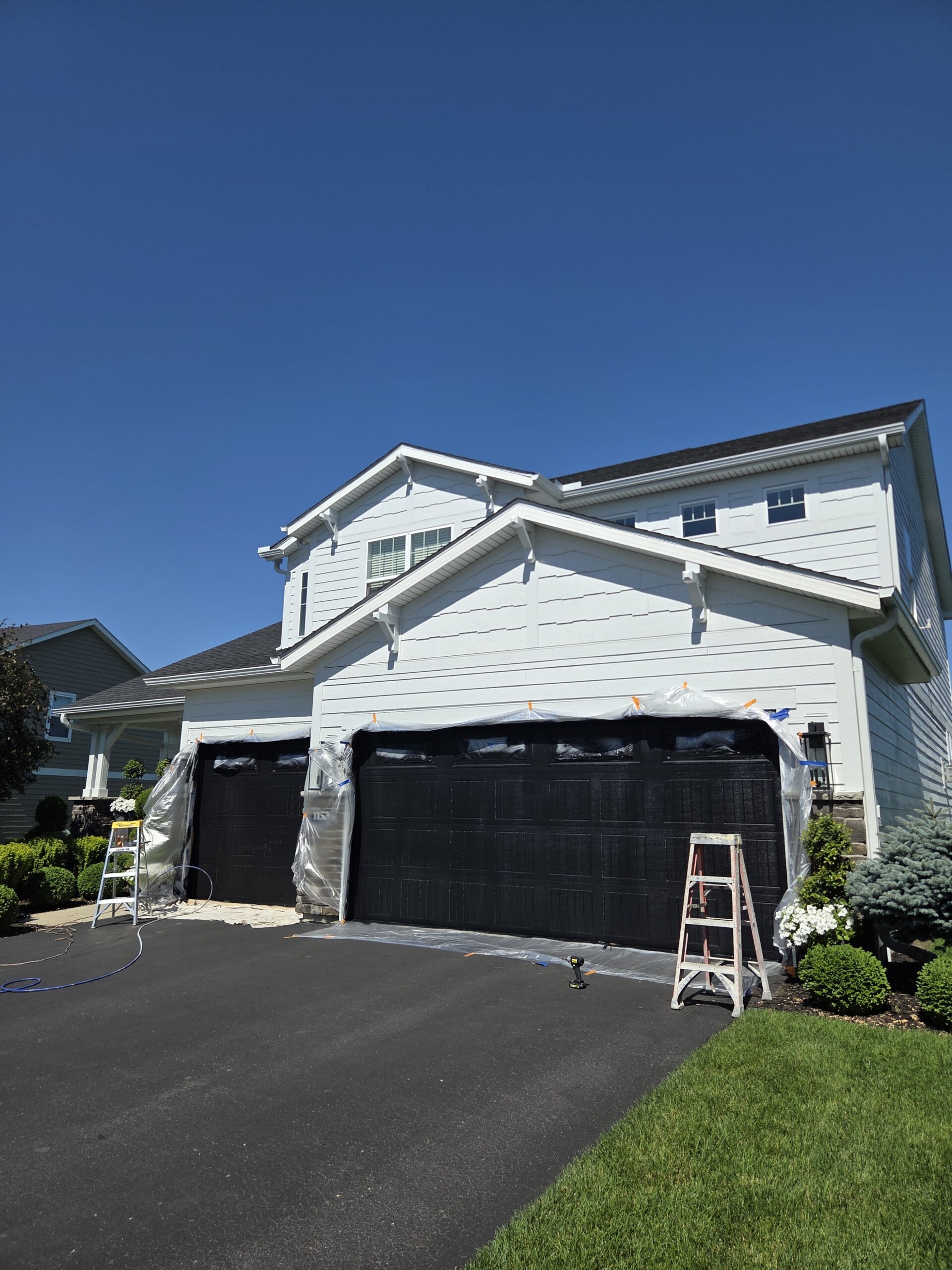 Garage doors and driveway masked in plastic sheeting and tape with ladders staged before exterior spraying