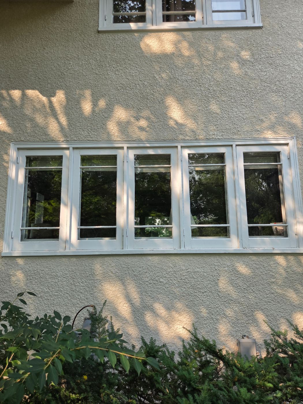Row of five casement windows with freshly painted white frames and sills on a stucco wall