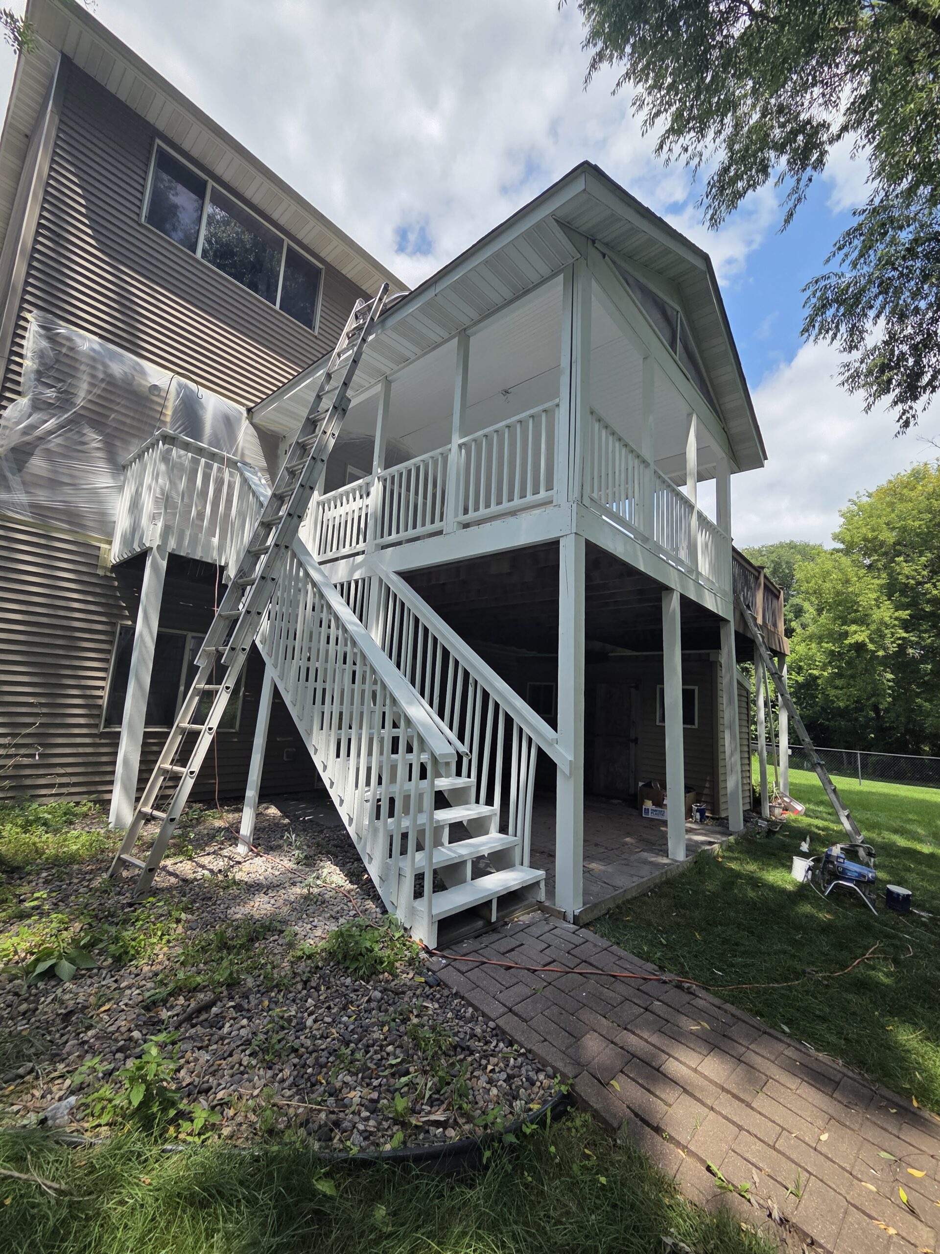 House siding and upper deck wrapped in plastic sheeting while the porch railings and staircase are coated