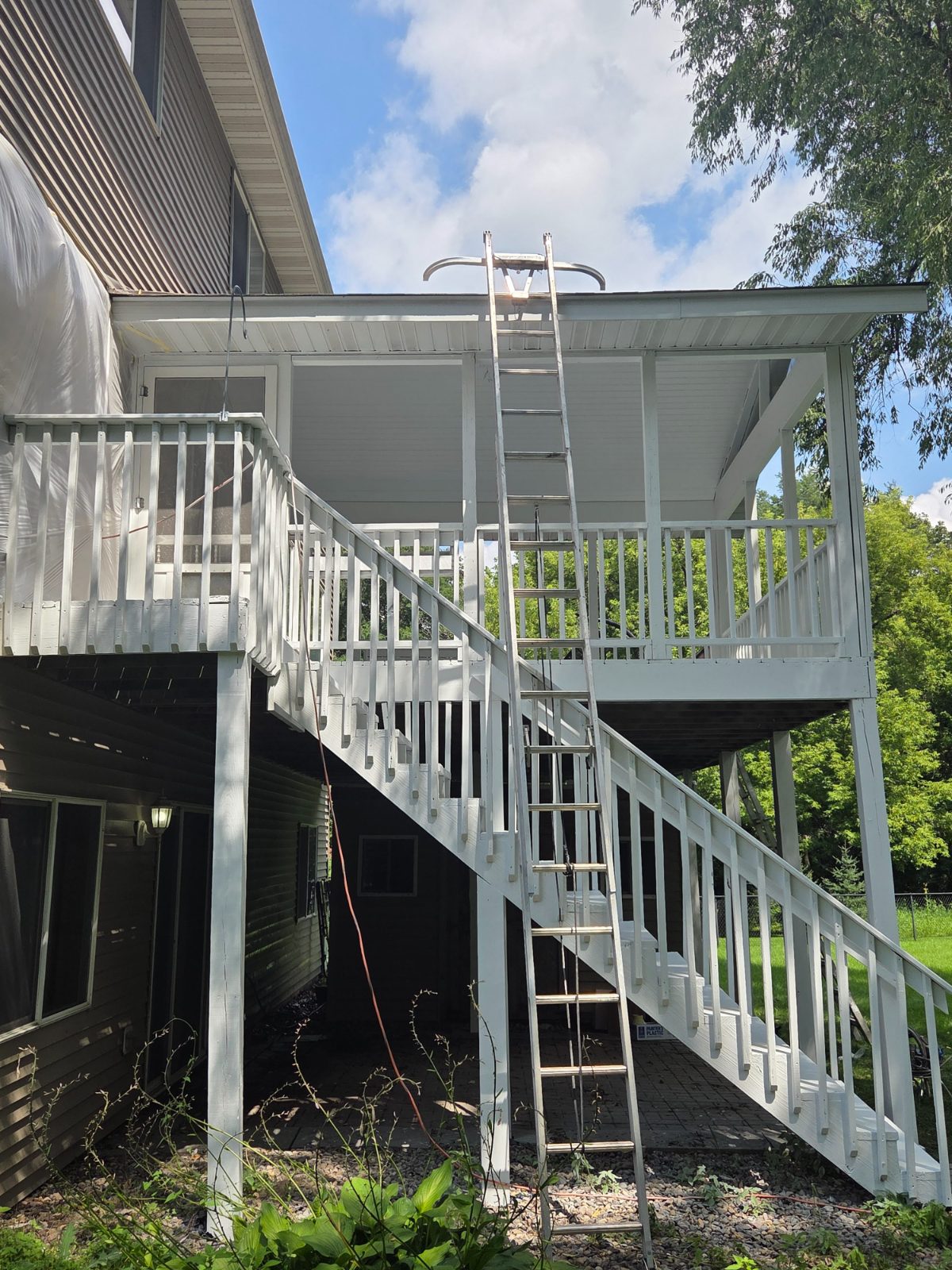 House wall wrapped in plastic while the attached porch and staircase are painted white