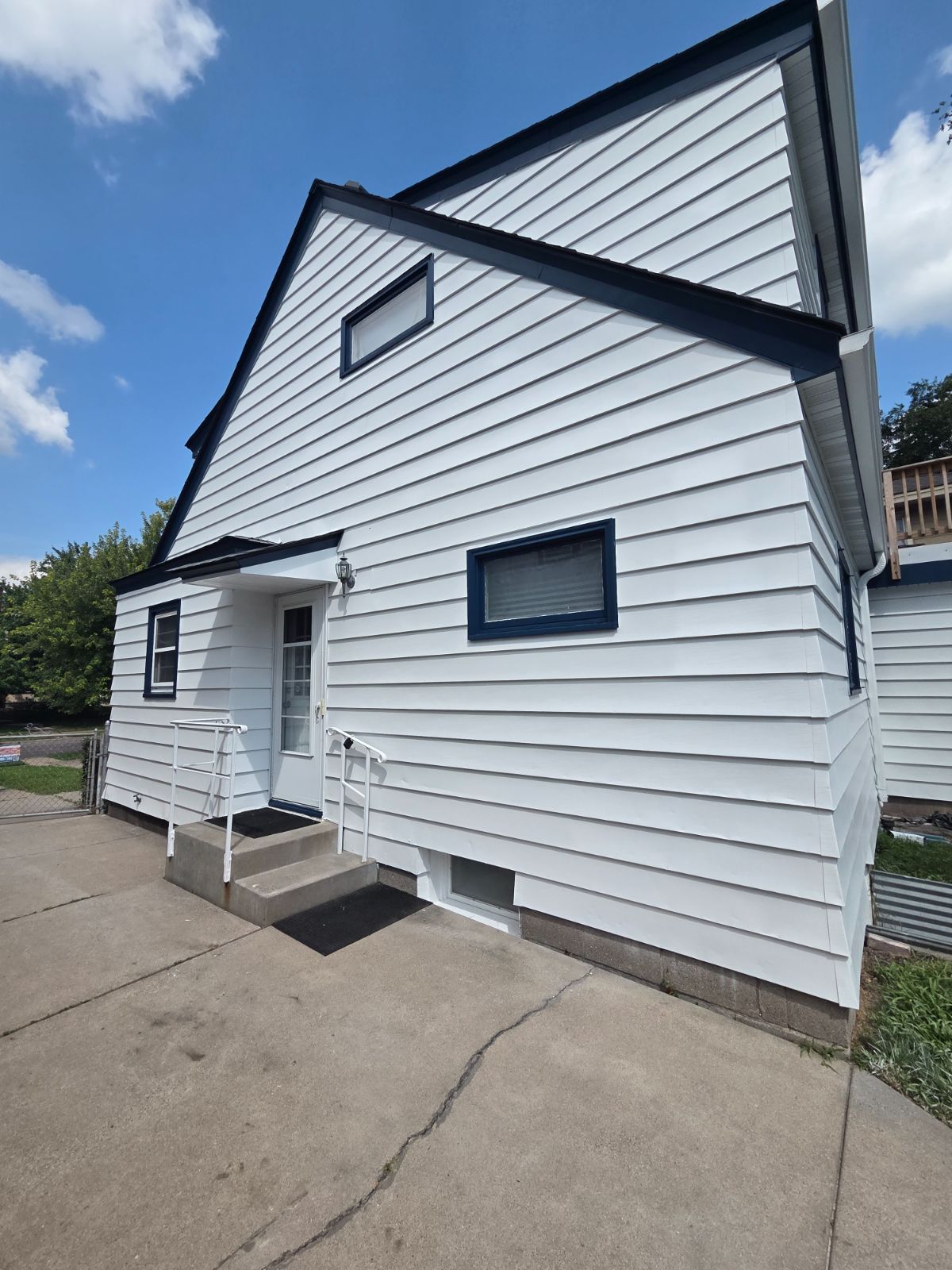Side of a home repainted white with navy trim around windows, eaves, and the entry canopy